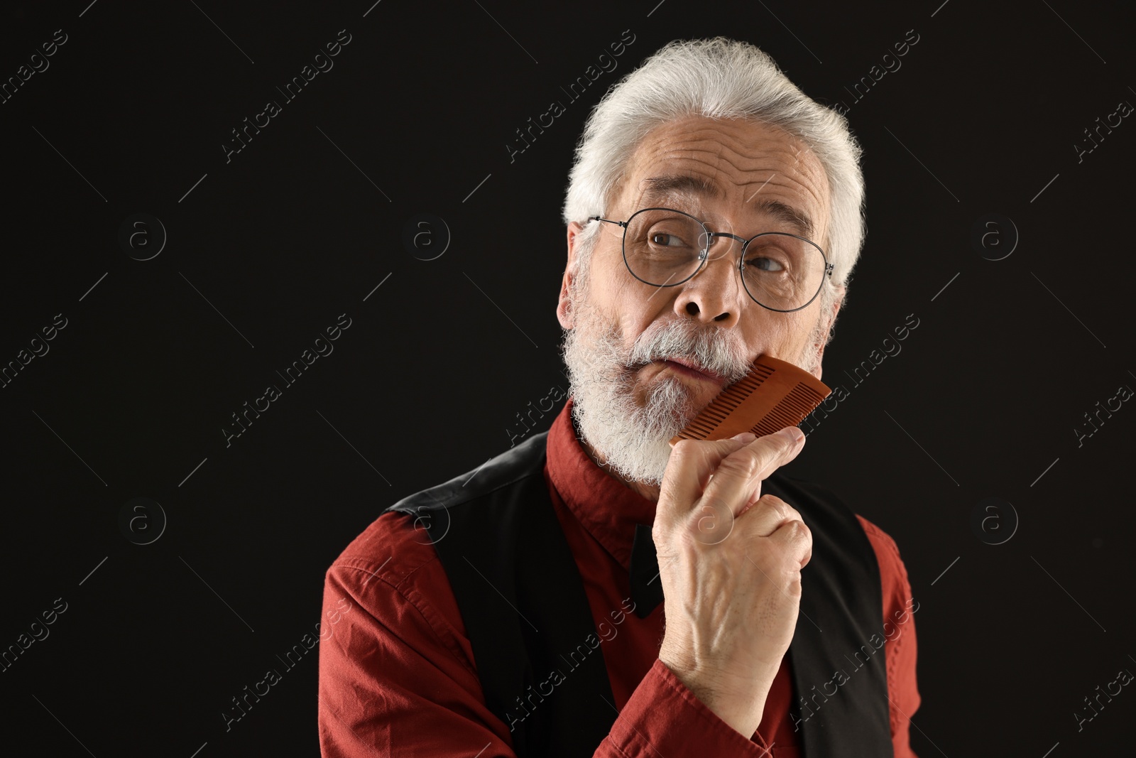 Photo of Senior man combing mustache on black background