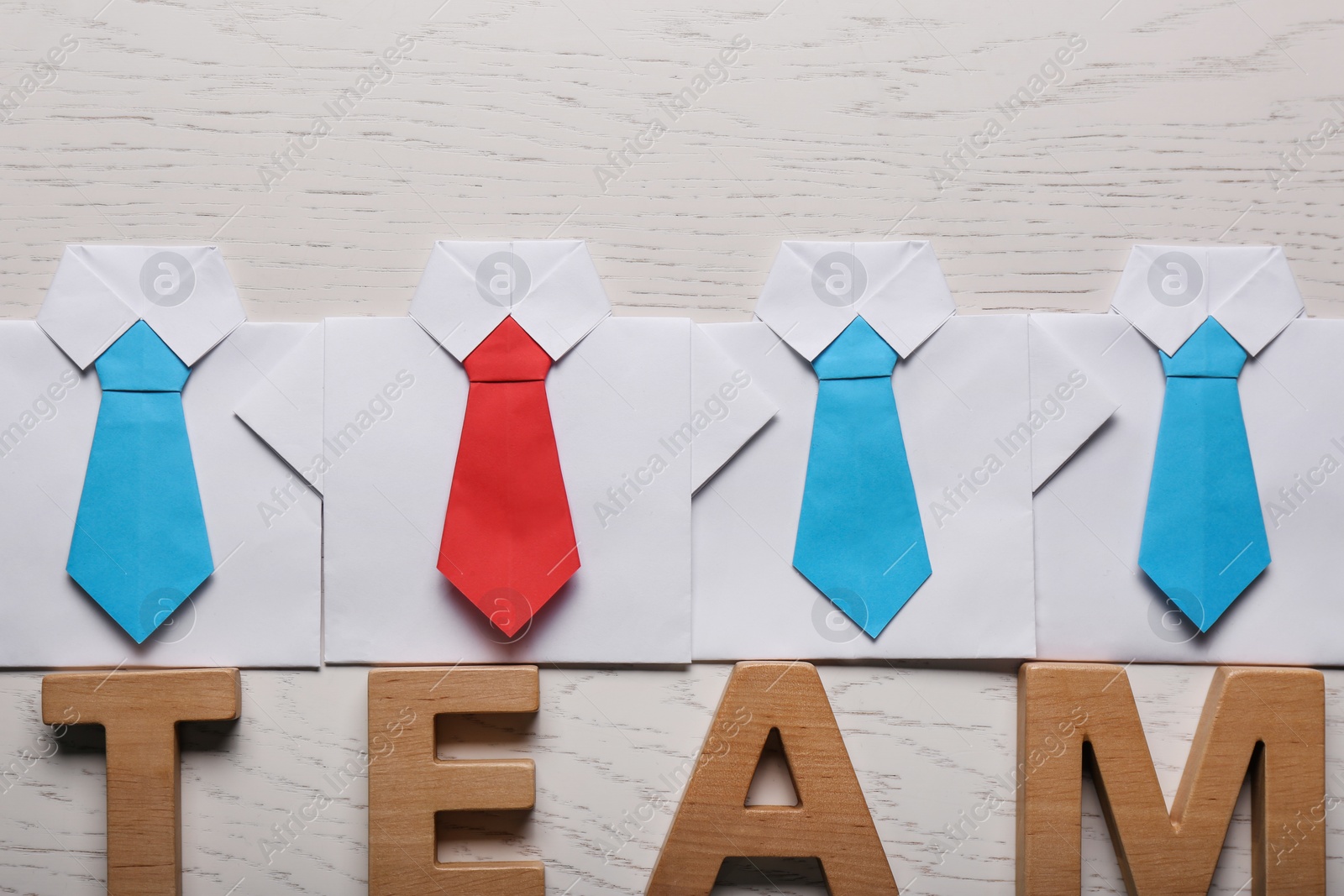 Photo of Many paper shirts and word Team on white wooden background, flat lay. Recruiter searching employee