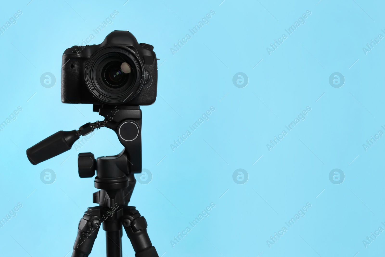 Photo of Modern tripod with professional camera on light blue background. Space for text