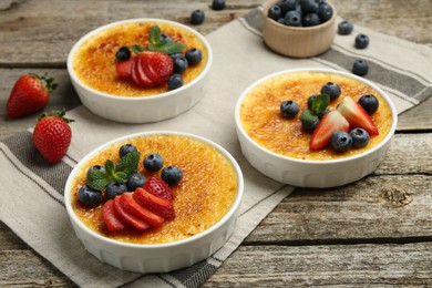 Photo of Delicious creme brulee with berries and mint in bowls on wooden table, closeup