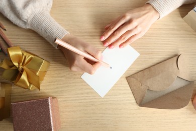 Photo of Woman writing message in greeting card on wooden table, top view
