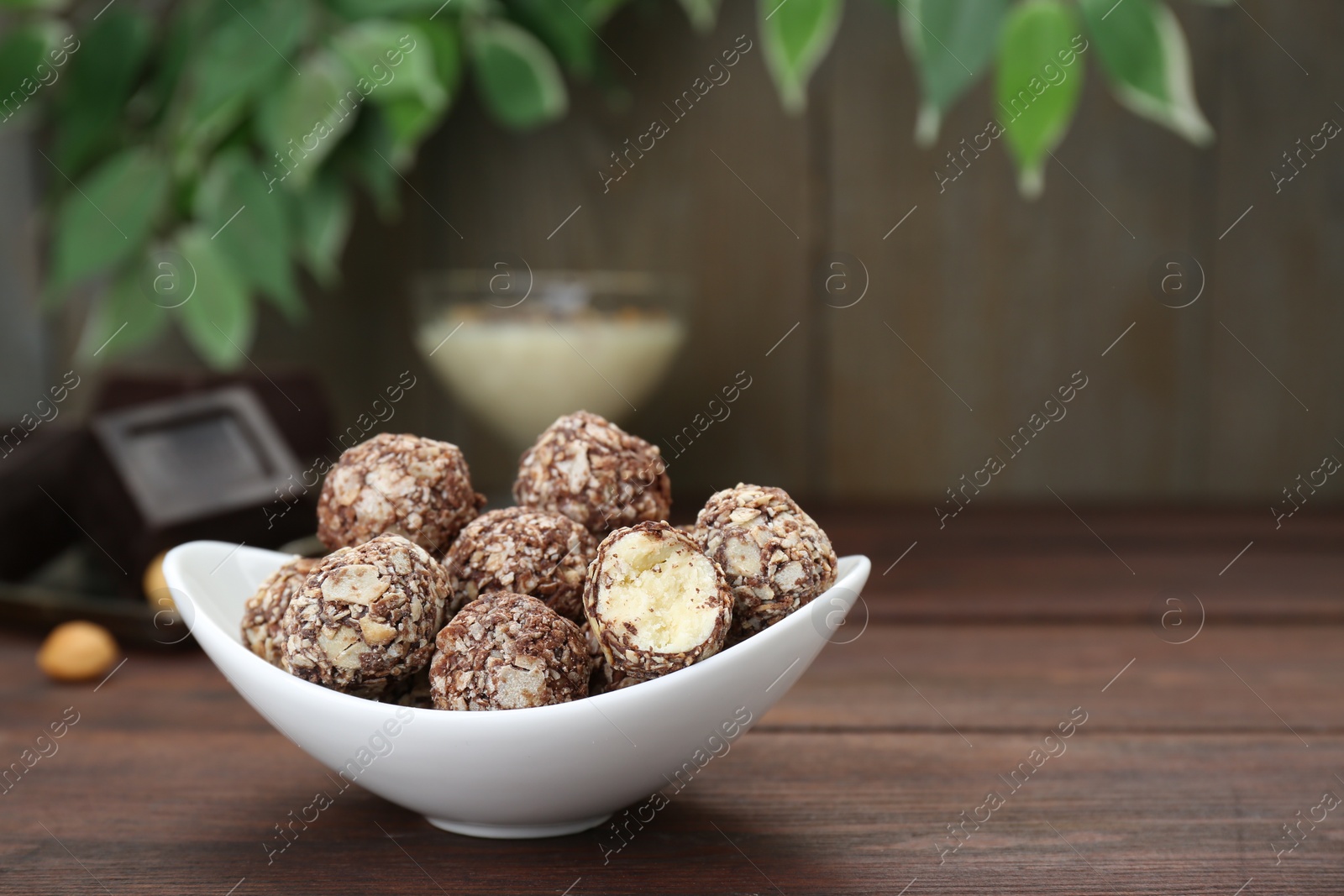 Photo of Bowl of delicious sweet chocolate candies on wooden table, space for text