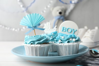 Photo of Delicious cupcakes with light blue cream and toppers for baby shower on white wooden table