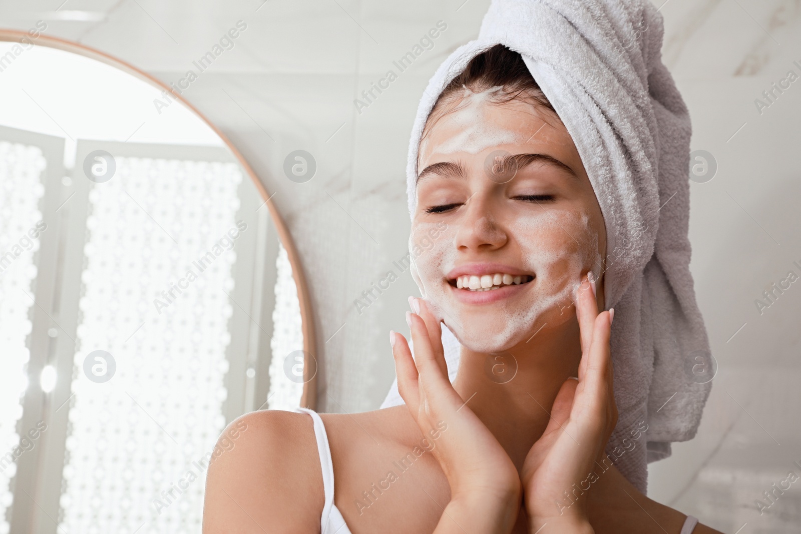 Photo of Beautiful teenage girl applying cleansing foam onto face in bathroom, space for text. Skin care cosmetic