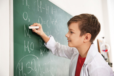 Photo of Schoolboy writing chemical formulas on chalkboard in classroom