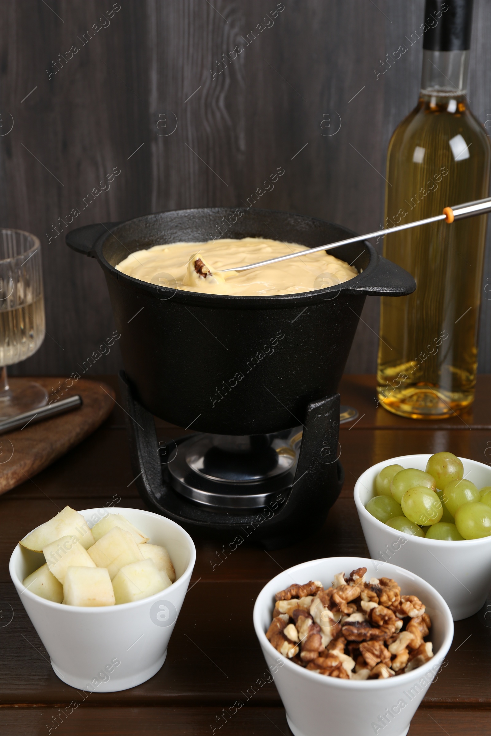 Photo of Fondue pot with tasty melted cheese, fork, wine and different snacks on wooden table