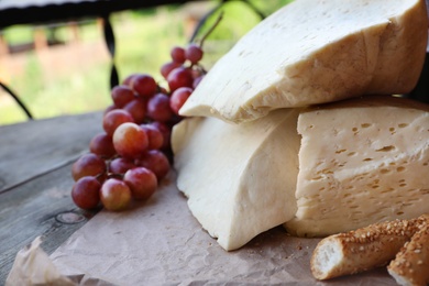 Photo of Delicious cheese, bread and ripe grape on wooden table, closeup