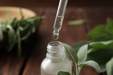 Photo of Dripping herbal essential oil from pipette into bottle on wooden table, closeup