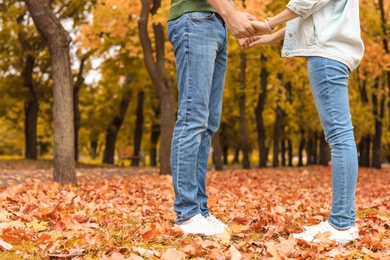 Photo of Couple standing on ground covered with leaves in park. Autumn walk