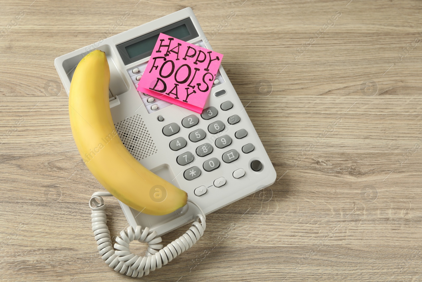 Photo of Corded phone with banana as handset and words Happy Fool's Day on wooden table, above view. Space for text