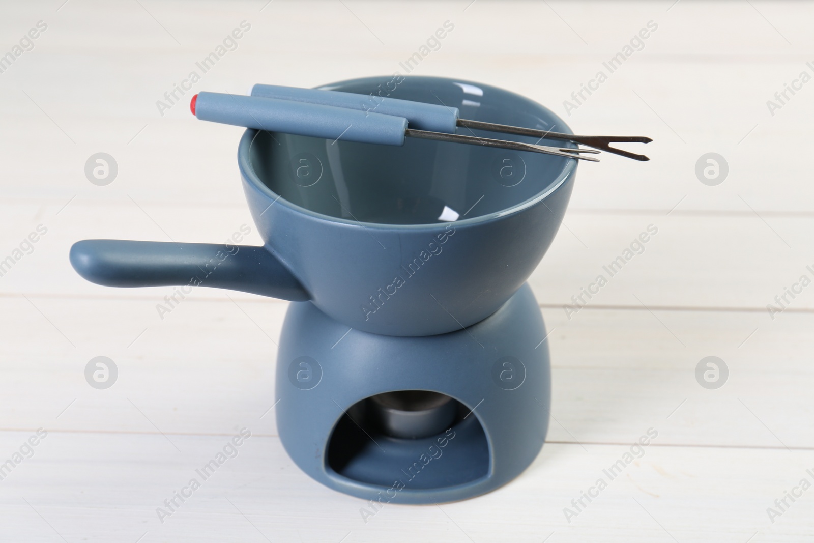 Photo of Fondue set on white wooden table, closeup