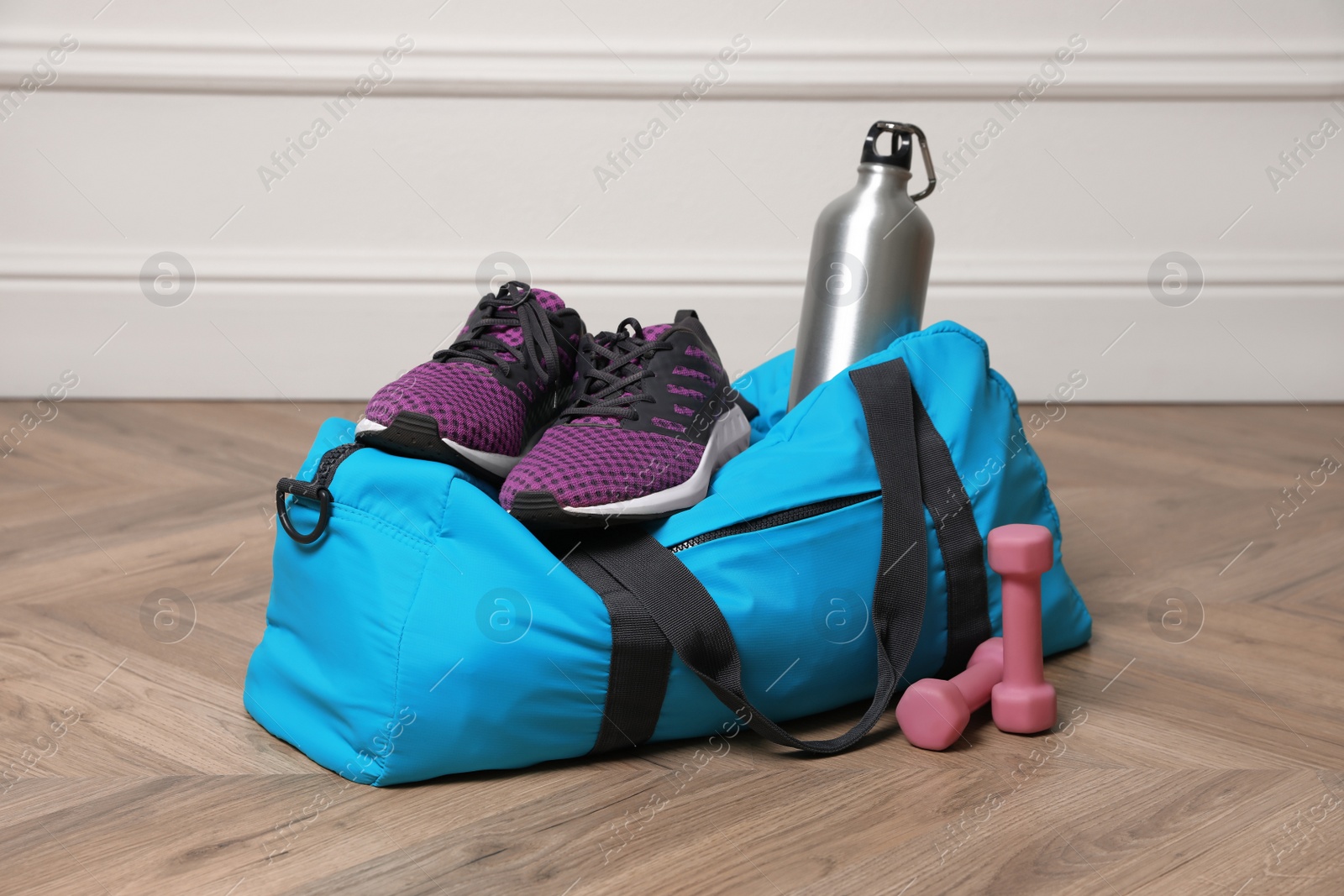 Photo of Blue gym bag with sports accessories on floor near white wall indoors