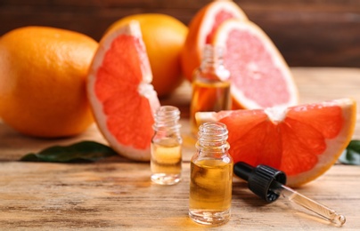 Bottles of essential oil, pipette and grapefruits on wooden table, space for text