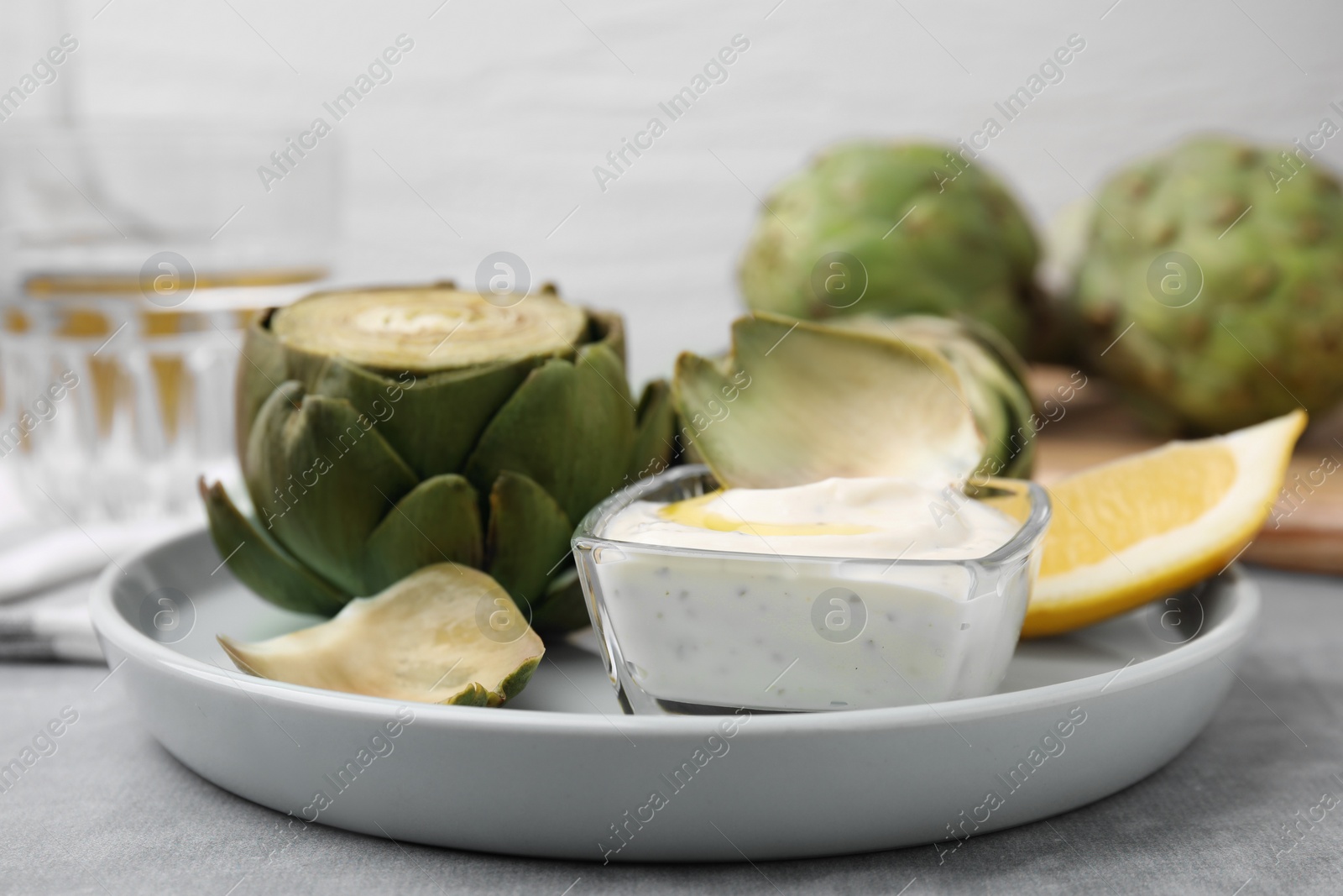 Photo of Delicious cooked artichokes with tasty sauce served on grey table, closeup