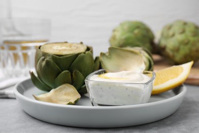 Delicious cooked artichokes with tasty sauce served on grey table, closeup