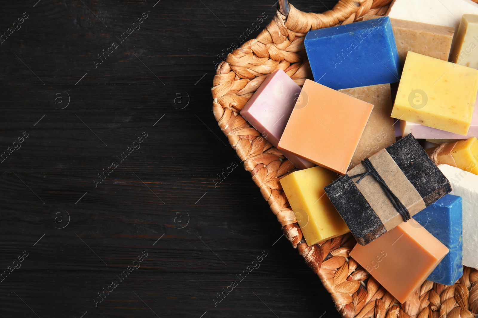 Photo of Many different handmade soap bars in wicker basket and space for text on table, top view