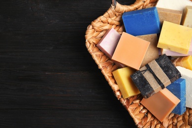 Many different handmade soap bars in wicker basket and space for text on table, top view