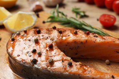 Tasty salmon steak with peppercorns on wooden table, closeup view