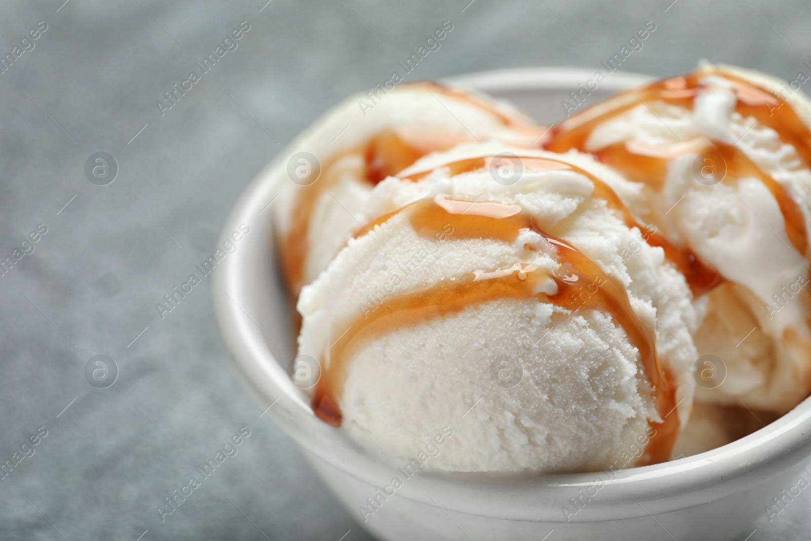 Photo of Tasty ice cream with caramel sauce in bowl on table, closeup