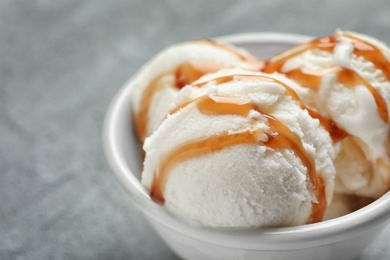 Tasty ice cream with caramel sauce in bowl on table, closeup