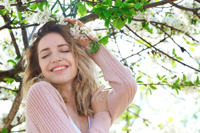 Attractive young woman posing near blossoming tree on sunny spring day