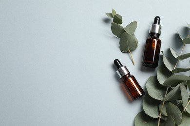 Aromatherapy. Bottles of essential oil and eucalyptus branches on grey background, flat lay. Space for text