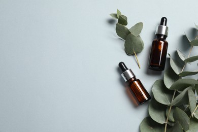 Photo of Aromatherapy. Bottles of essential oil and eucalyptus branches on grey background, flat lay. Space for text