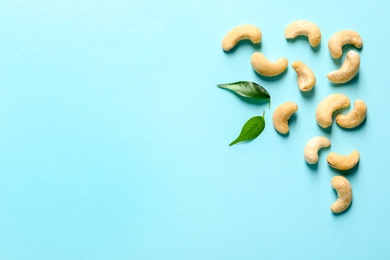 Photo of Tasty cashew nuts and leaves on color background, top view. Space for text