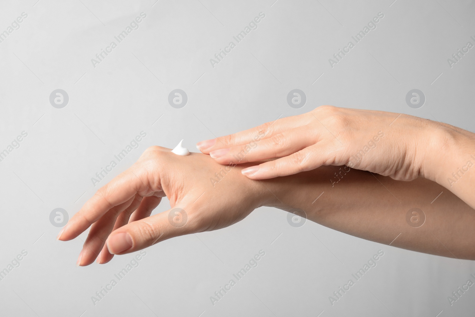 Photo of Woman applying hand cream on light background, closeup