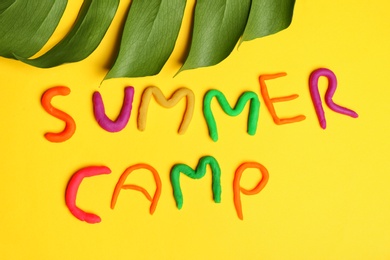 Photo of Flat lay composition with words SUMMER CAMP made from modelling clay and tropical leaf on color background