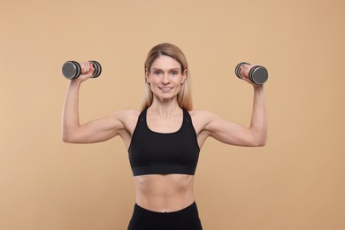Photo of Portrait of athletic woman exercising with dumbbells on beige background