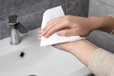 Woman wiping hands with paper towel in bathroom, closeup