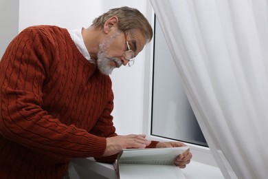 Upset senior man with book near window at home. Loneliness concept