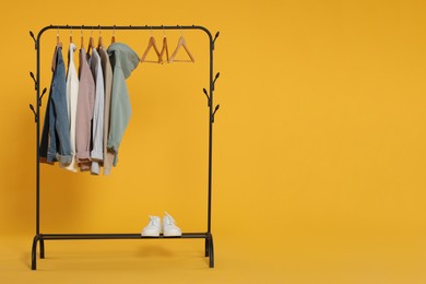 Photo of Rack with stylish clothes on wooden hangers against orange background, space for text