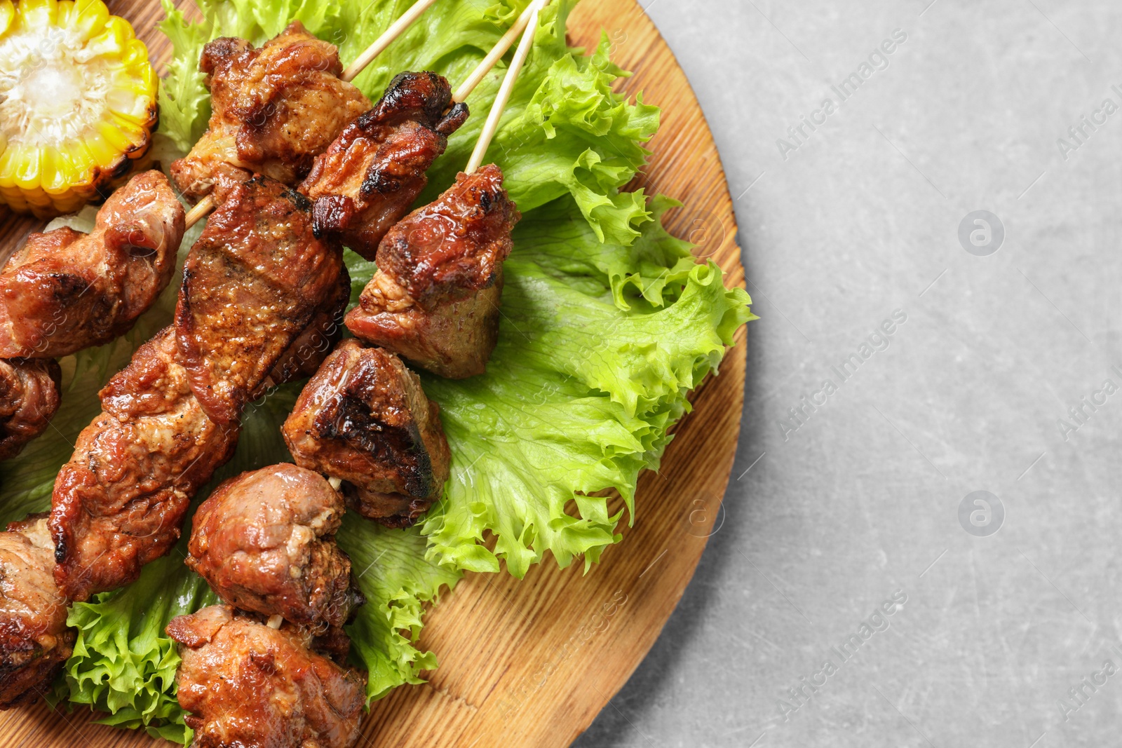 Photo of Wooden board with barbecued meat and garnish on grey background, top view. Space for text