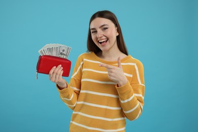 Photo of Happy woman pointing at wallet with dollar banknotes on light blue background