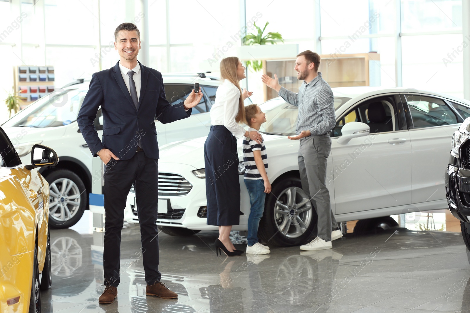 Photo of Salesman with key and young family in car salon