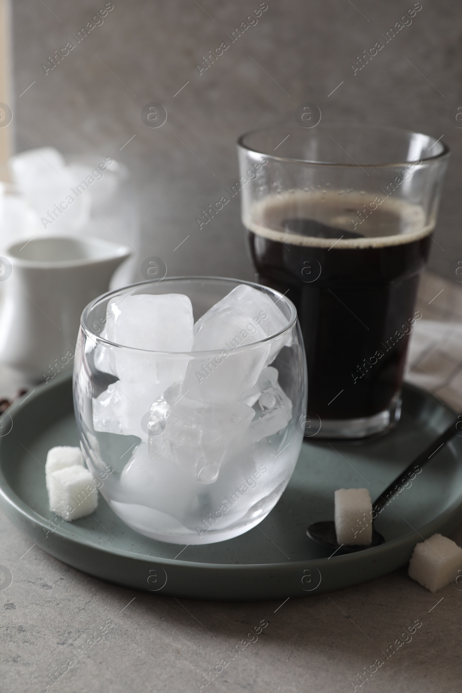 Photo of Making iced coffee. Ice cubes in glass, ingredients and spoon on gray table