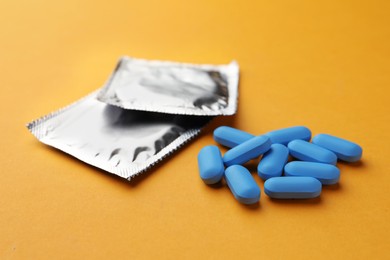 Photo of Pills and condoms on orange background. Potency problem