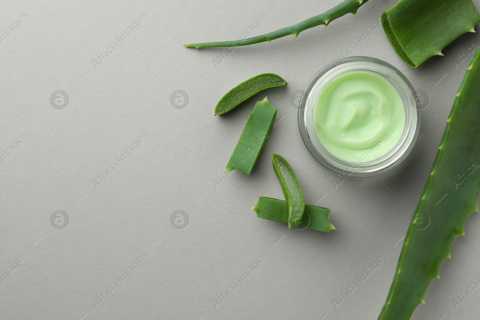 Photo of Jar with cream and cut aloe leaves on light grey background, flat lay. Space for text