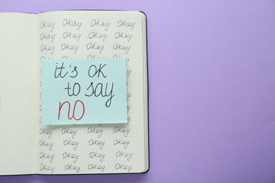 Photo of Card with phrase It`s Ok to Say No in notebook on violet background, top view. Space for text