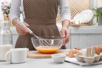 Photo of Woman whisking eggs in bowl at table indoors, closeup