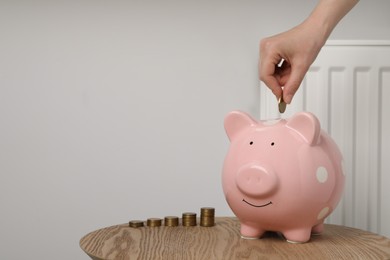 Photo of Woman putting coin into piggy bank near heating radiator, closeup. Space for text