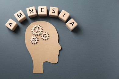 Wooden cubes with word Amnesia, human head cutout and cogwheels on grey background, top view. Space for text