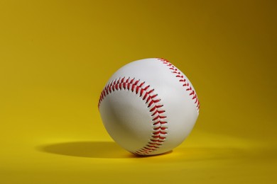 Photo of One baseball ball with stitches on yellow background
