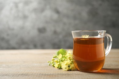 Photo of Cup of tea and linden blossom on wooden table. Space for text