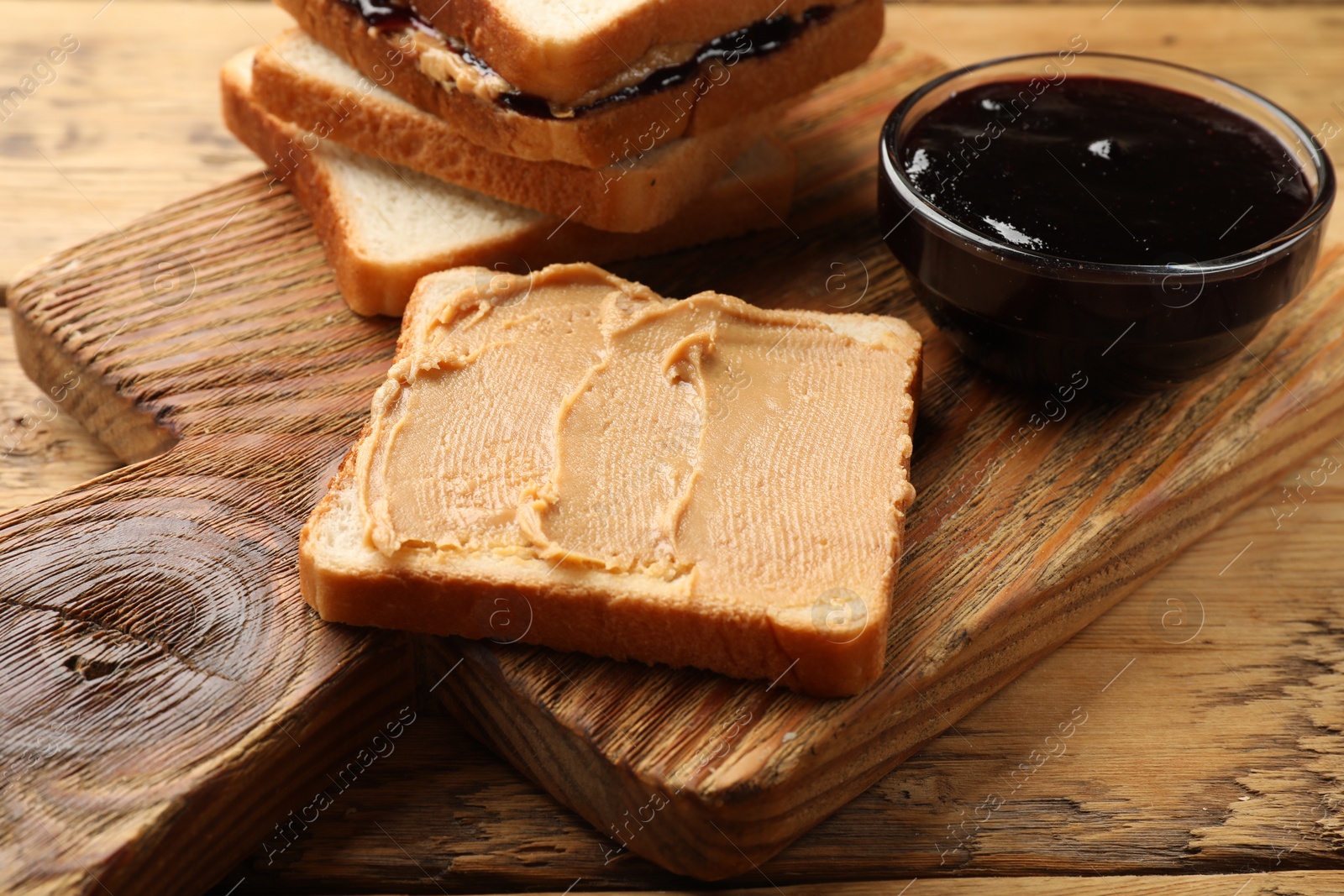 Photo of Tasty peanut butter sandwiches and jam on wooden table, closeup