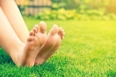 Woman sitting barefoot on fresh green grass outdoors, closeup. Space for text