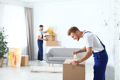 Photo of Moving service employee sealing cardboard box with adhesive tape in room