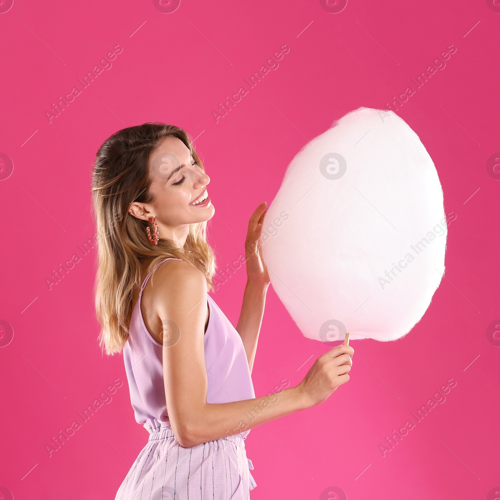 Photo of Happy young woman with cotton candy on pink background